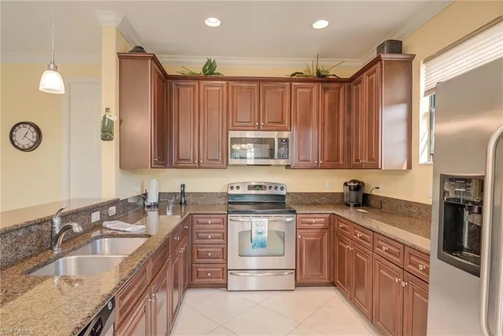 Kitchen featuring stainless steel appliances, light stone countertops, crown molding, light tile patterned floors, and pendant lighting