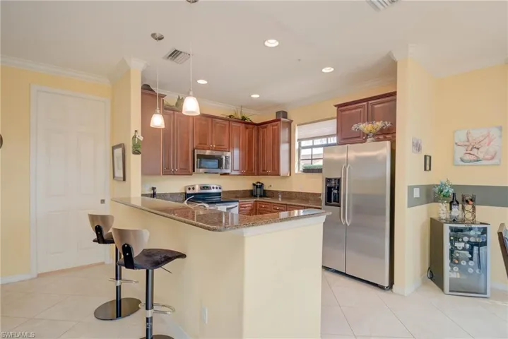 Kitchen with stainless steel appliances,  stone counters, a breakfast bar area, light tile patterned flooring, and hanging light fixtures