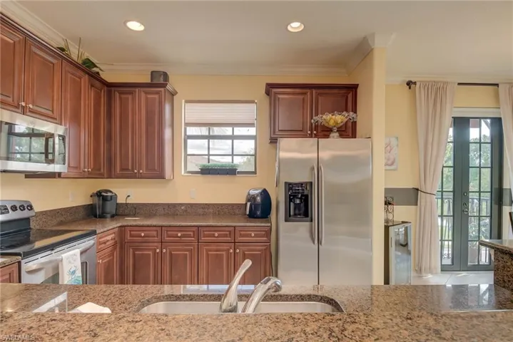 Kitchen with stainless steel appliances, dark stone countertops, crown molding, recessed lighting, and french doors