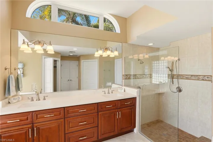 Primary ensuite bathroom featuring double vanity with quartz countertop, tiled shower, a high ceiling, and light tile patterned floors
