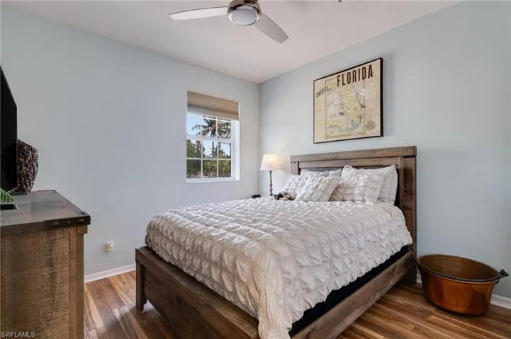 Bedroom featuring wood-finish flooring, a window with outdoor tree scenery, and a ceiling fan
