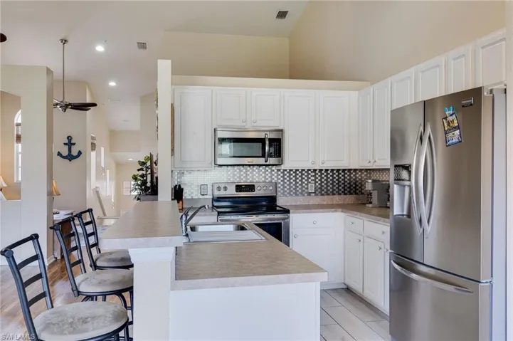 Kitchen featuring white cabinetry, stainless steel appliances, a bar-height counter, a mosaic tile backsplash, and light-toned countertops