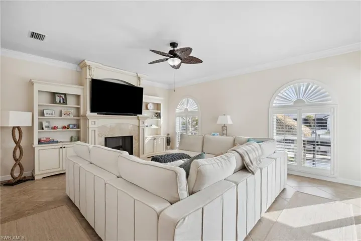 Tiled living room with ceiling fan, a healthy amount of sunlight, ornamental molding, and a fireplace