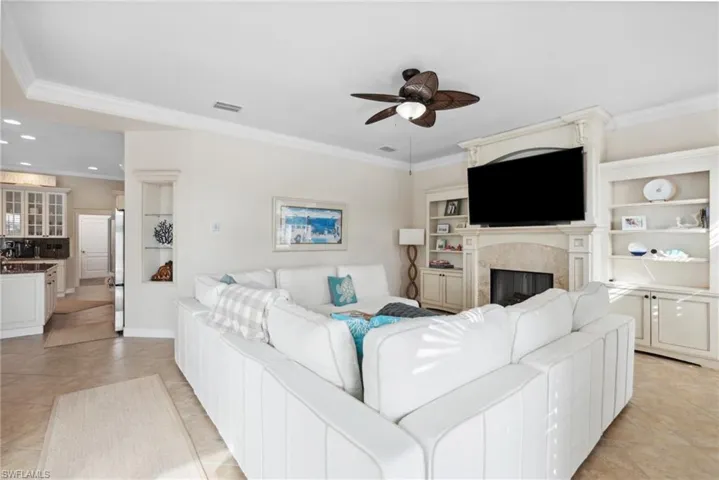 Tiled living room featuring ceiling fan, ornamental molding, and a fireplace