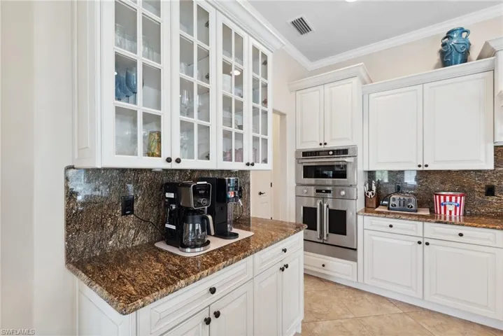 Kitchen with double oven, dark stone countertops, decorative backsplash, and white cabinets
