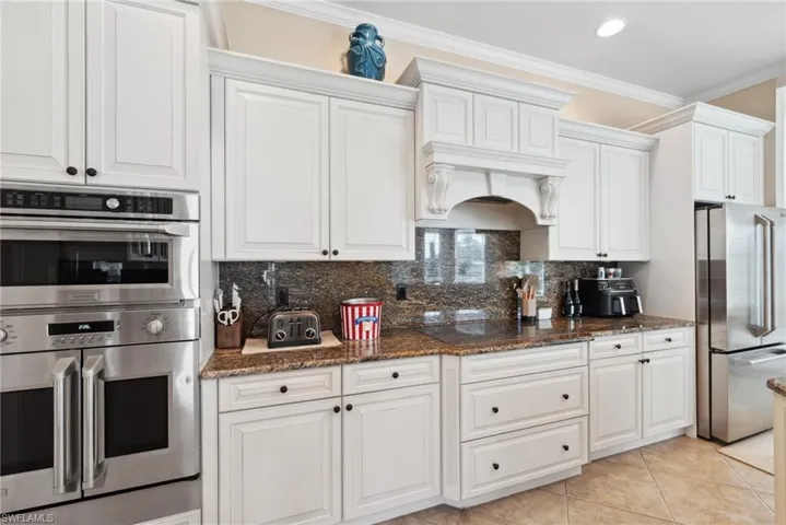 Kitchen featuring decorative backsplash, dark stone countertops, white cabinetry, and appliances with stainless steel finishes