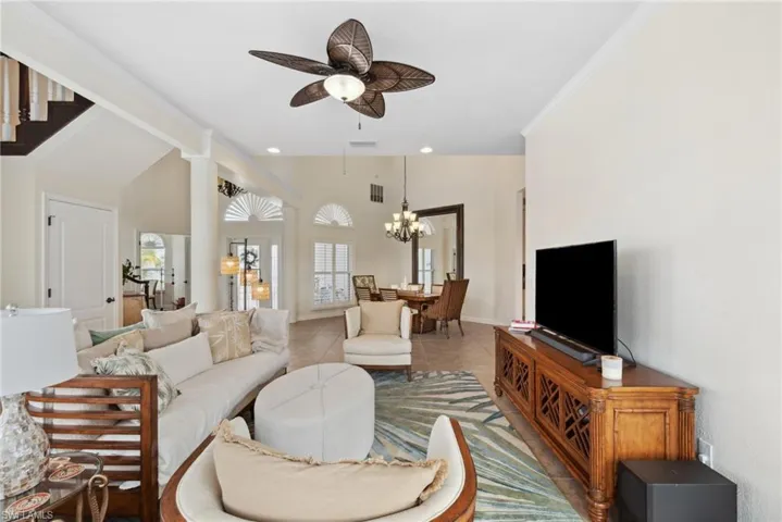 Tiled living room featuring ceiling fan with notable chandelier and ornamental molding