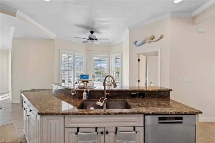 Kitchen with sink, light tile patterned floors, stainless steel dishwasher, dark stone countertops, and white cabinets