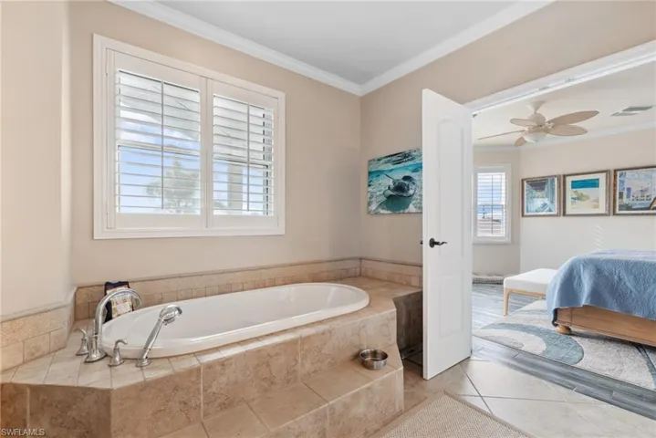 Bathroom featuring tile patterned floors, ceiling fan, a relaxing tiled tub, and crown molding