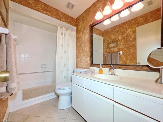 Full bathroom with vanity, shower / bath combo with shower curtain, light tile patterned floors, and wallpapered walls
