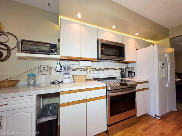 Kitchen featuring stainless steel appliances, a textured ceiling, white cabinets, tasteful backsplash, and light countertops