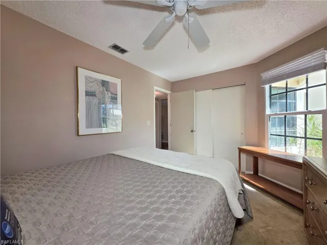 Carpeted bedroom with a textured ceiling, a closet, and a ceiling fan