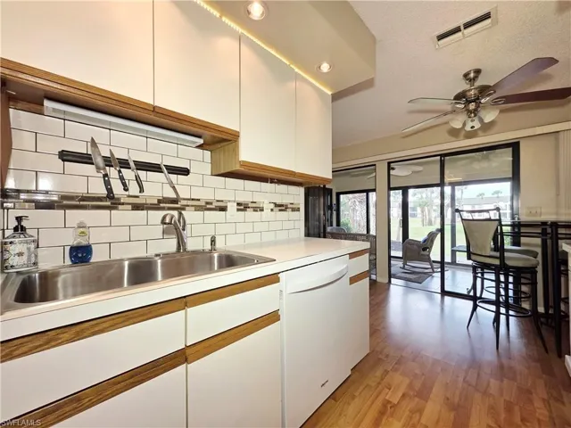 Kitchen featuring tasteful backsplash, light countertops, dishwasher, light wood-style floors, and white cabinetry