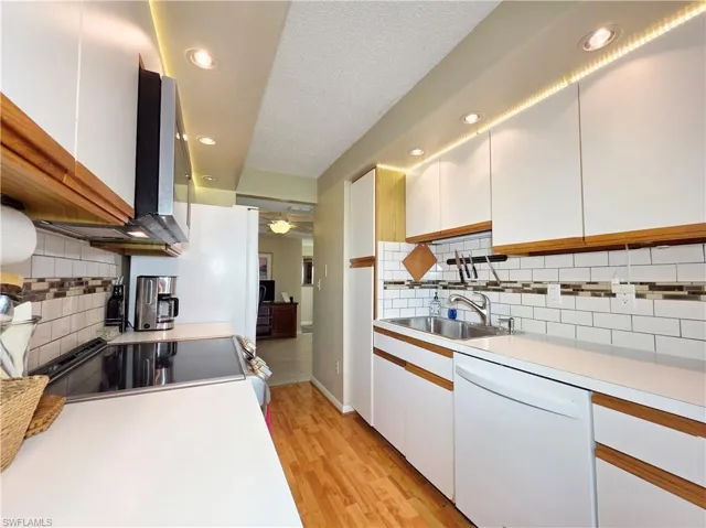 Kitchen with white cabinets, light countertops, white appliances, decorative backsplash, and light wood-type flooring