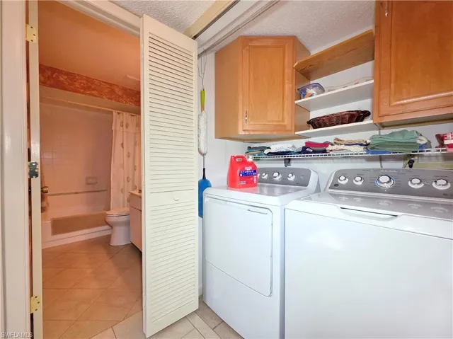 Washroom featuring a textured ceiling, cabinet space, light tile patterned flooring, and washing machine and clothes dryer