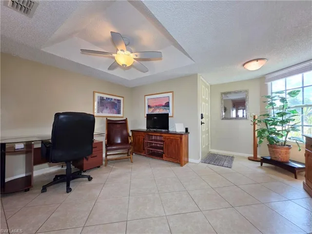Office area featuring a textured ceiling, light tile patterned floors, a ceiling fan, and a raised ceiling