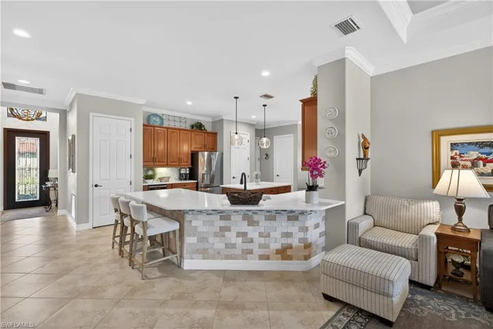 Kitchen featuring wood finish cabinetry, a kitchen bar, a center island, hanging light fixtures, and stainless steel refrigerator with ice dispenser