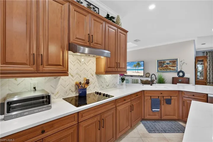 Kitchen featuring wood finish cabinets, light stone countertops, crown molding, black electric cooktop, and light tile patterned floors