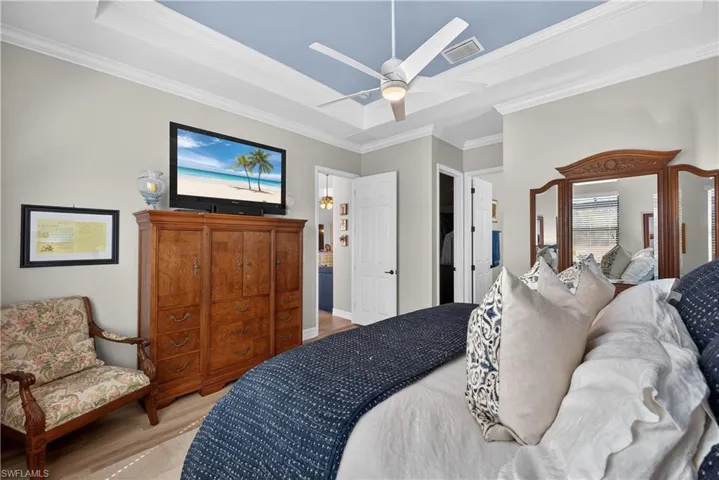 Bedroom with light wood-style flooring, ceiling fan, ornamental molding, and a raised ceiling