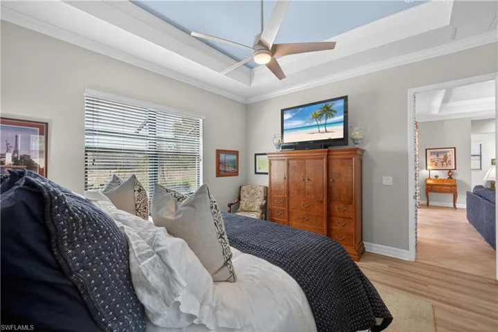 Bedroom featuring a raised ceiling, crown molding, wood finished floors, and a ceiling fan