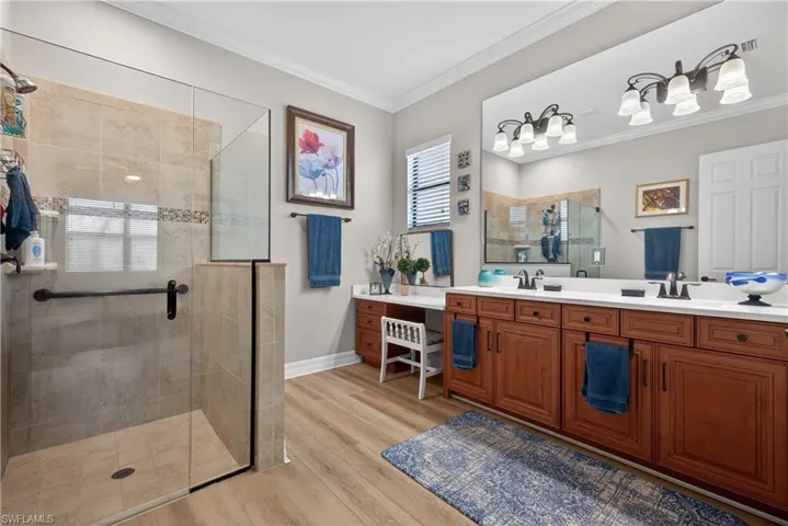 Bathroom featuring crown molding, double vanity, a shower stall, and light wood-style flooring