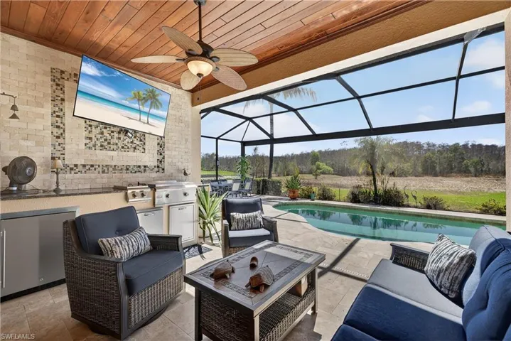 View of patio featuring glass enclosure, a sunroom, an outdoor pool, a ceiling fan, and an outdoor kitchen and area to lounge