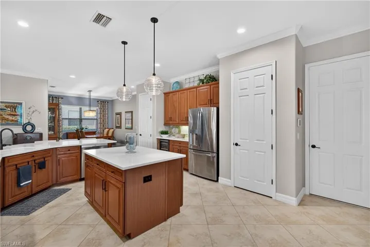 Kitchen featuring wood finish cabinetry, crown molding, stainless steel appliances, decorative light fixtures, and light tile patterned floors