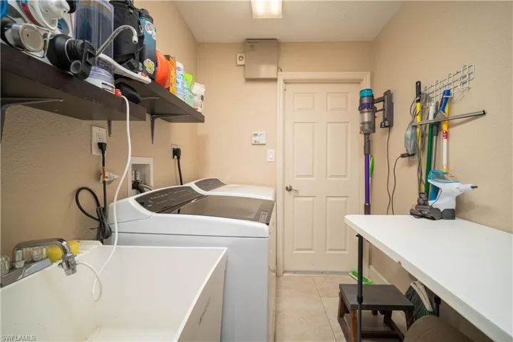 Clothes washing area featuring sink, separate washer and dryer, and light tile patterned floors