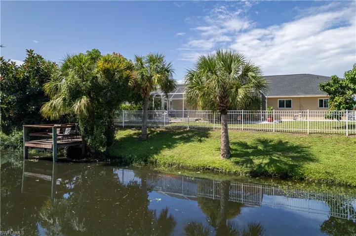 Dock area with glass enclosure, a water view, and a lawn