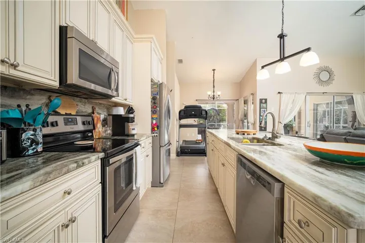 Kitchen featuring appliances with stainless steel finishes, backsplash, sink, light stone countertops, and light tile patterned flooring