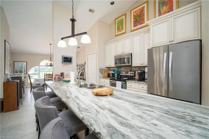 Kitchen with appliances with stainless steel finishes, decorative backsplash, an inviting chandelier, and light stone countertops