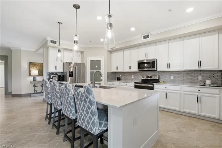 Kitchen with stainless steel appliances, white cabinetry, a kitchen breakfast bar, light stone counters, and crown molding