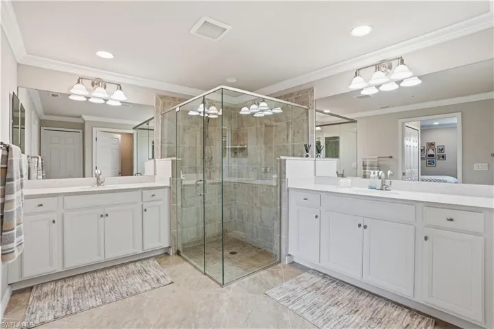 Bathroom featuring ornamental molding, two vanities, a shower stall, and ensuite bathroom