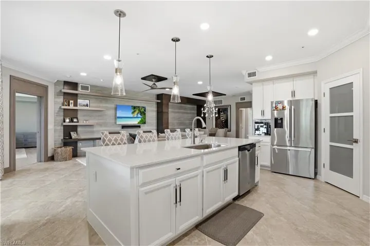 Kitchen featuring white cabinets, a center island with sink, stainless steel appliances, ornamental molding, and light stone countertops