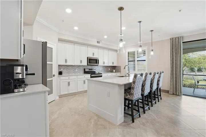 Kitchen featuring light stone counters, a breakfast bar, white cabinetry, an island with sink, and ornamental molding