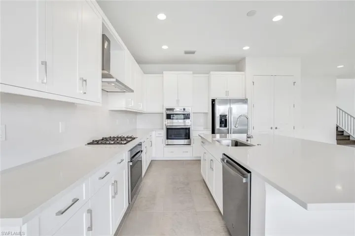 Kitchen with white cabinets, stainless steel appliances, sink, wall chimney exhaust hood, and a center island with sink