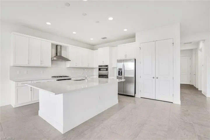 Kitchen featuring white cabinetry, stainless steel appliances, an island with sink, sink, and wall chimney range hood