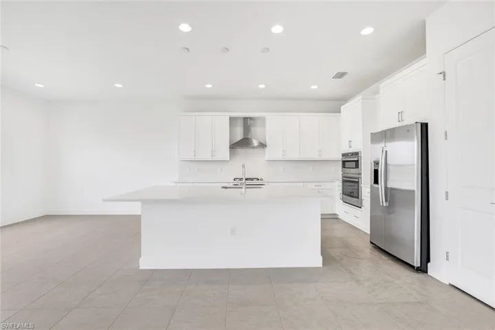 Kitchen featuring a kitchen island with sink, wall chimney exhaust hood, stainless steel appliances, and white cabinets