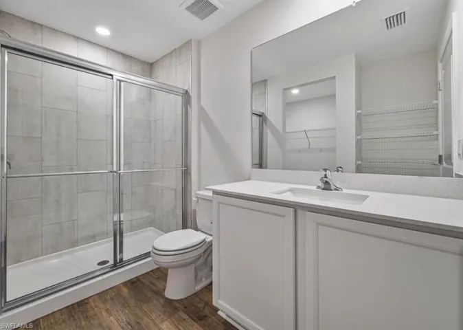 Full bath featuring a walk in closet, vanity, a stall shower, wood finished floors, and recessed lighting