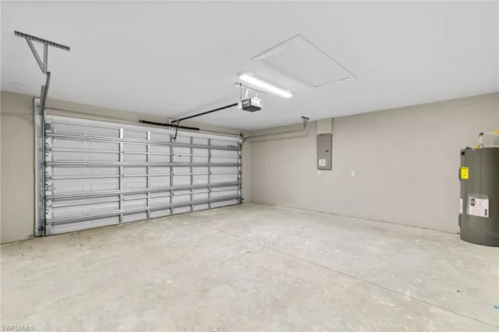 Garage with electric water heater, electric panel, and a garage door opener
