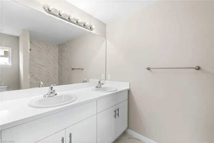 Bathroom with double vanity, marble look tiles, and a shower