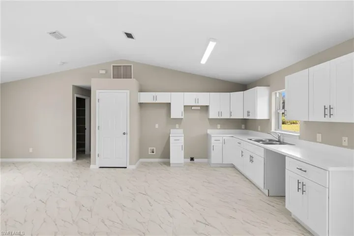Kitchen featuring vaulted ceiling, white cabinets, light marble finish floors, and light countertops