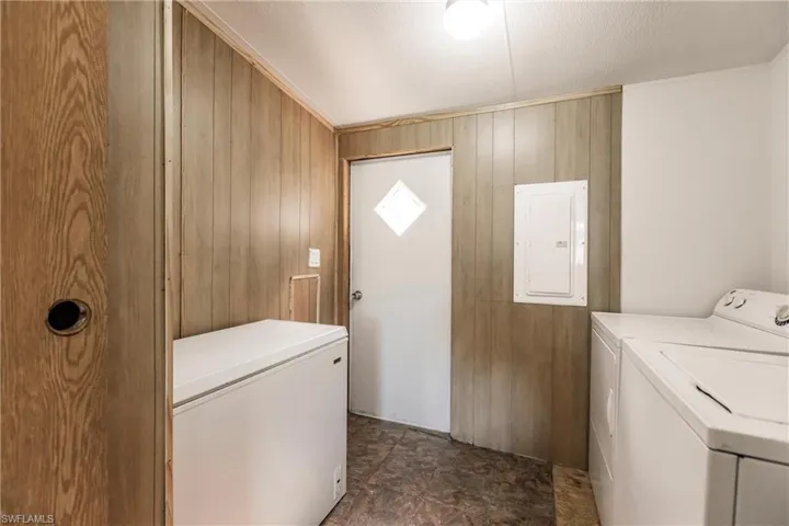 Clothes washing area with wooden walls, washer and dryer, dark tile patterned floors, and electric panel