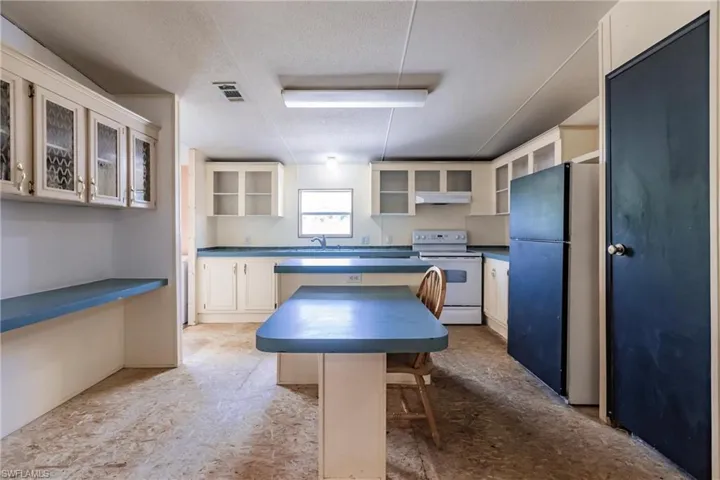 Kitchen featuring white cabinets, a breakfast bar, stainless steel refrigerator, white electric range oven, and a kitchen island