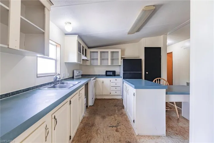 Kitchen with sink, white cabinetry, black appliances, and lofted ceiling