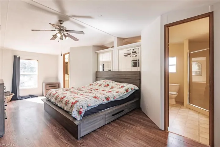 Bedroom with multiple windows, ensuite bath, ceiling fan, and hardwood / wood-style floors