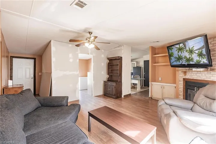Living room featuring built in features, a brick fireplace, light wood-type flooring, and ceiling fan