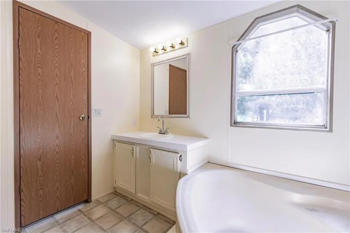 Bathroom featuring a healthy amount of sunlight, tile patterned floors, a tub to relax in, and vanity