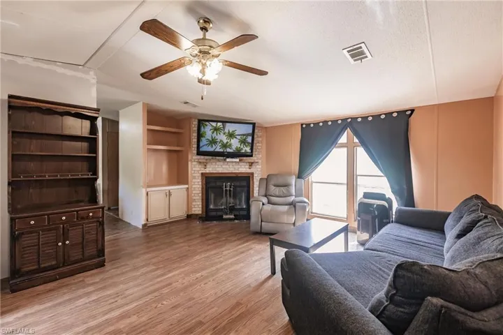 Living room with a fireplace, a textured ceiling, brick wall, ceiling fan, and wood-type flooring