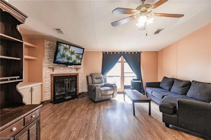 Living room with a fireplace, wood-type flooring, brick wall, and ceiling fan